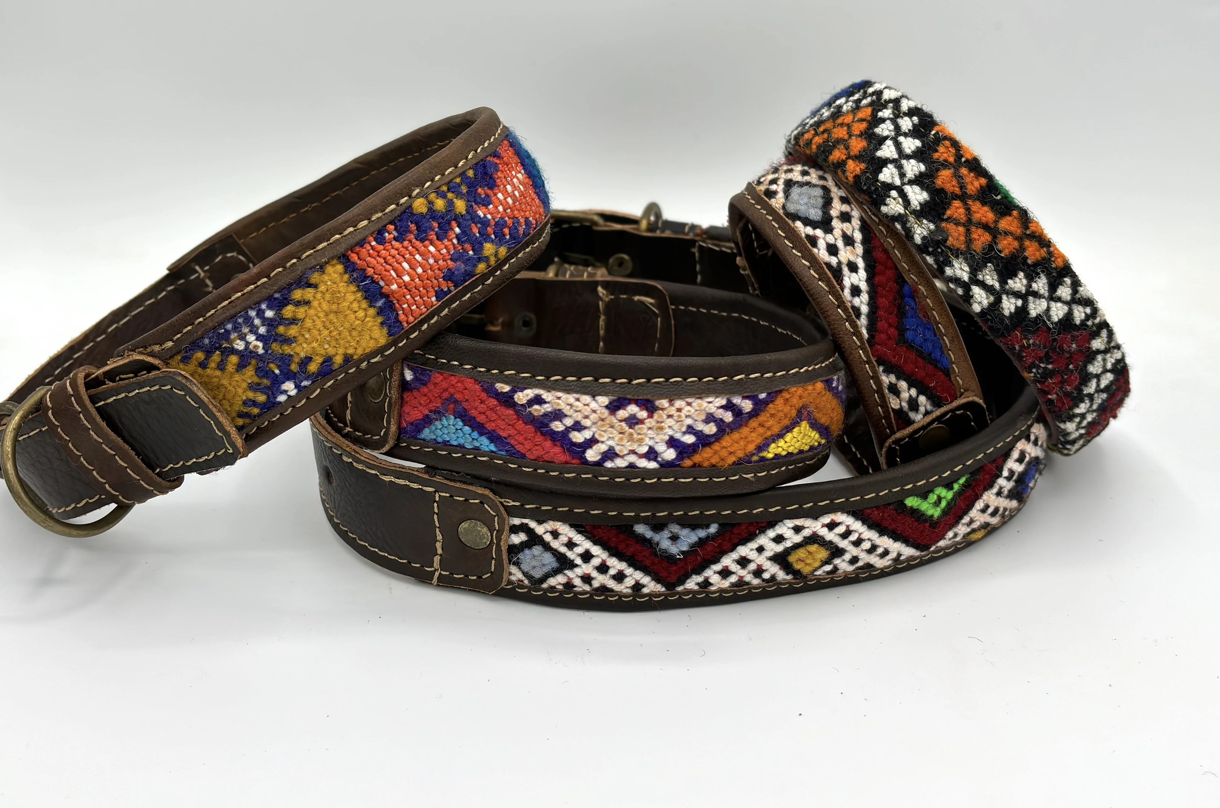 BohoBarks collars fanned across a white table, woven fronts in coral, saffron and cobalt
