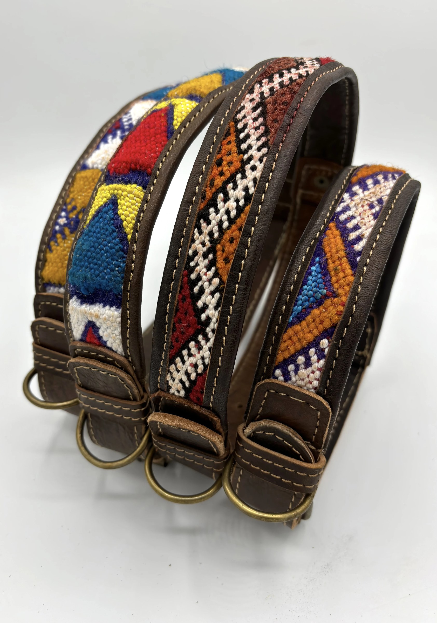 Four BohoBarks collars stacked upright, their hand-woven kilim fronts in red, saffron, cobalt and cream above brass D-rings