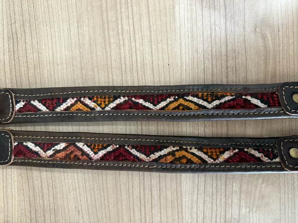 Two assorted kilim collars on a wood table, showing red, white and orange woven zigzags